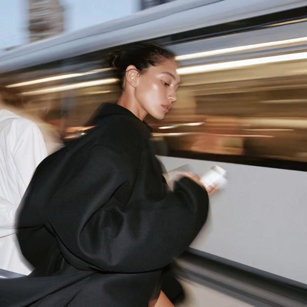 A woman in a black coat by a moving tram, reading her phone